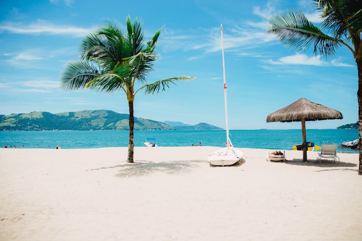 Tropical beach with palm trees, sailboat and umbrella — family-friendly Labor Day 2026 getaway