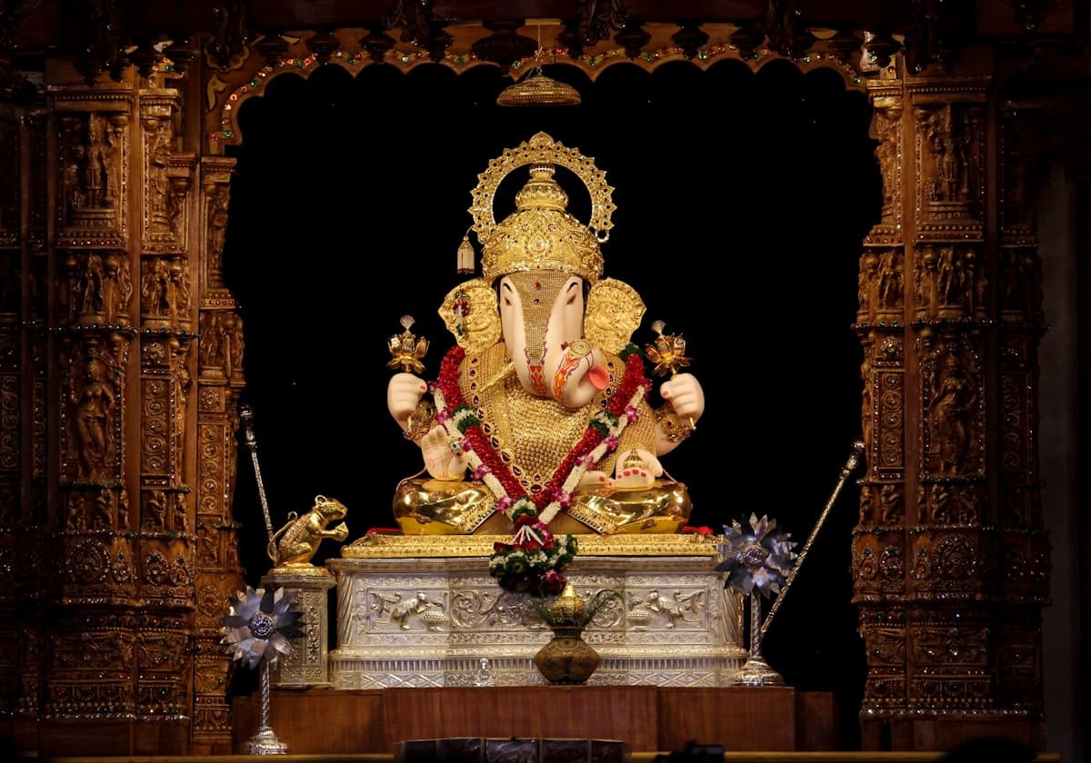 Golden Ganesha idol with flower garland in ornate wooden shrine — Ganesh Chaturthi 2026 temple